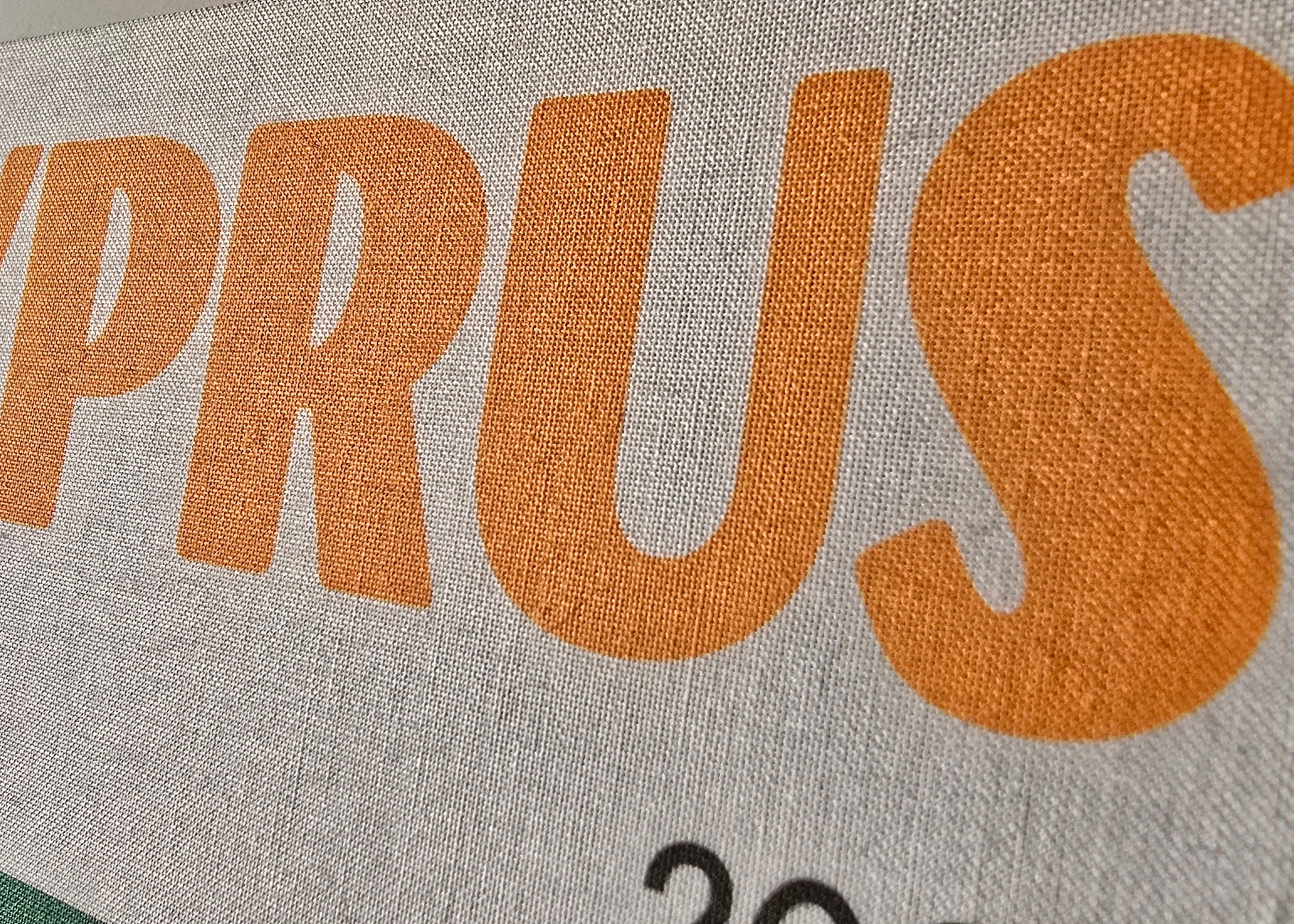 Text 'CYPRUS' printed on a fabric-like material with a neutral background