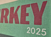 Green sign with 'TURKEY 2025' text on a fabric background