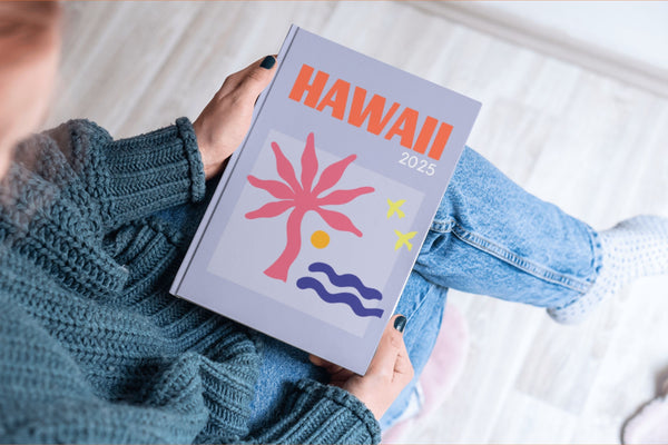 Person holding a travel guidebook with 'Hawaii 2025' on a blurred background
